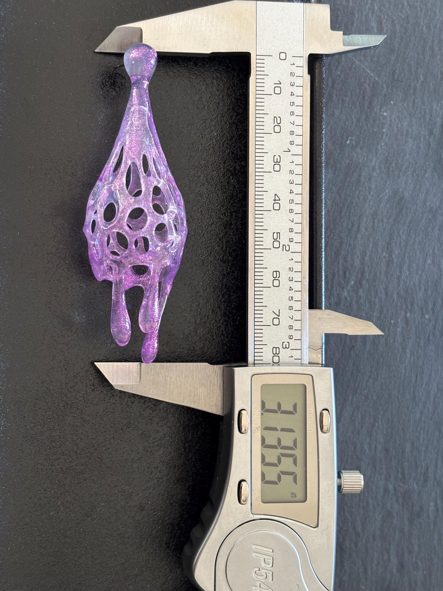 Purple dangling earrings being measured with a digital caliper on a dark background.