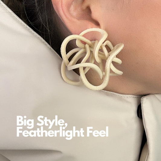 Side profile of model wearing cream statement earrings in a sculptural loop design.