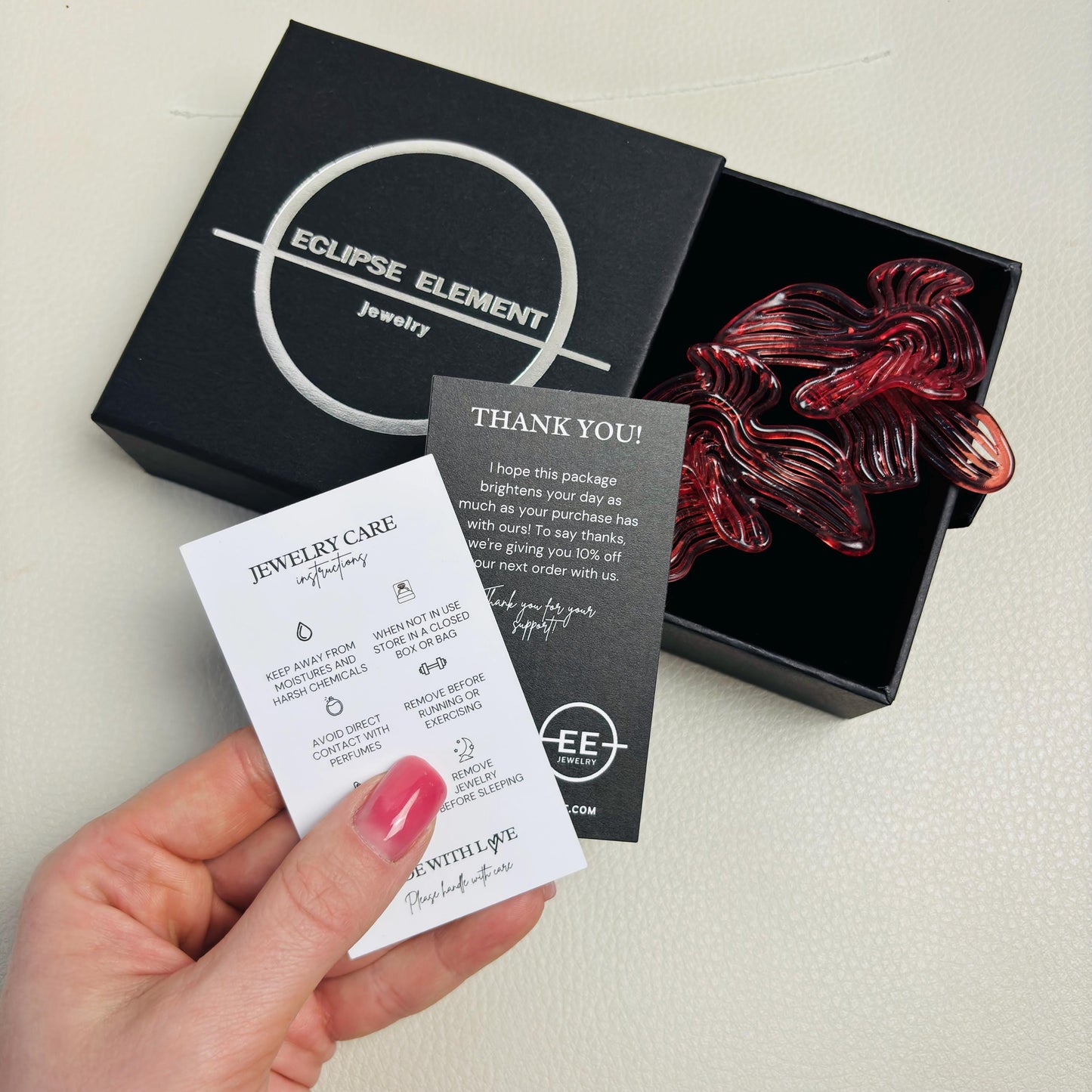 Hand holding the black gift box, thank you note, and Cherry Red Rhythm earrings