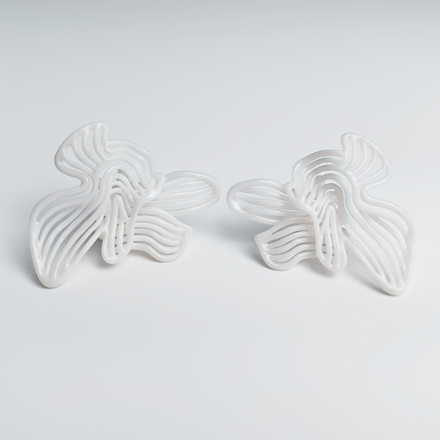 Two white butterfly-shaped earrings on a light gray background