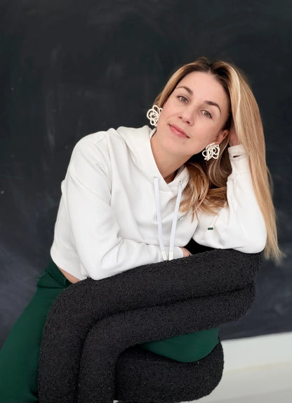 Woman wearing sculptural handcrafted earrings by Eclipse Element, seated on a modern black chair
