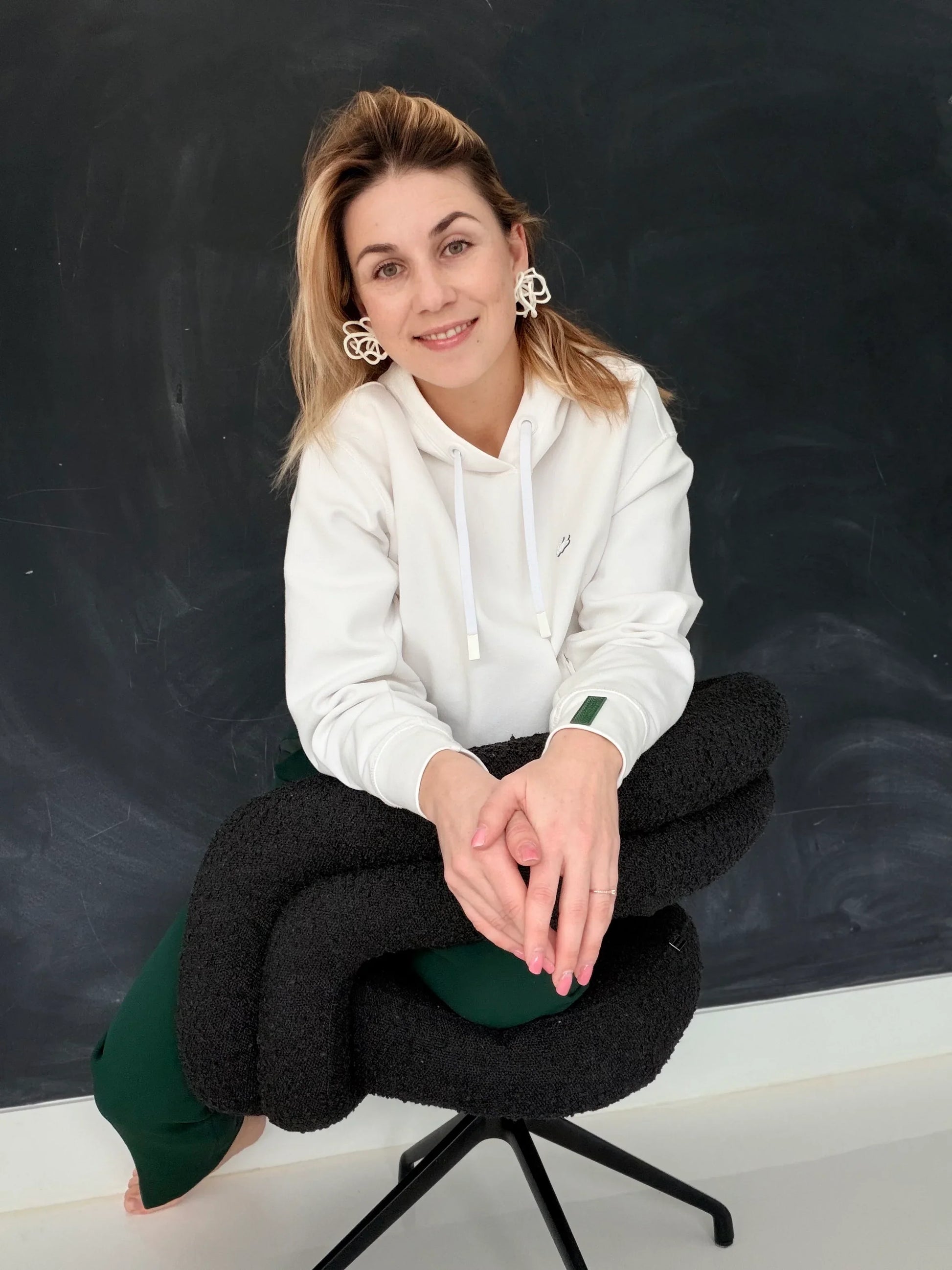 Woman wearing sculptural statement earrings from Eclipse Element, seated on a modern chair
