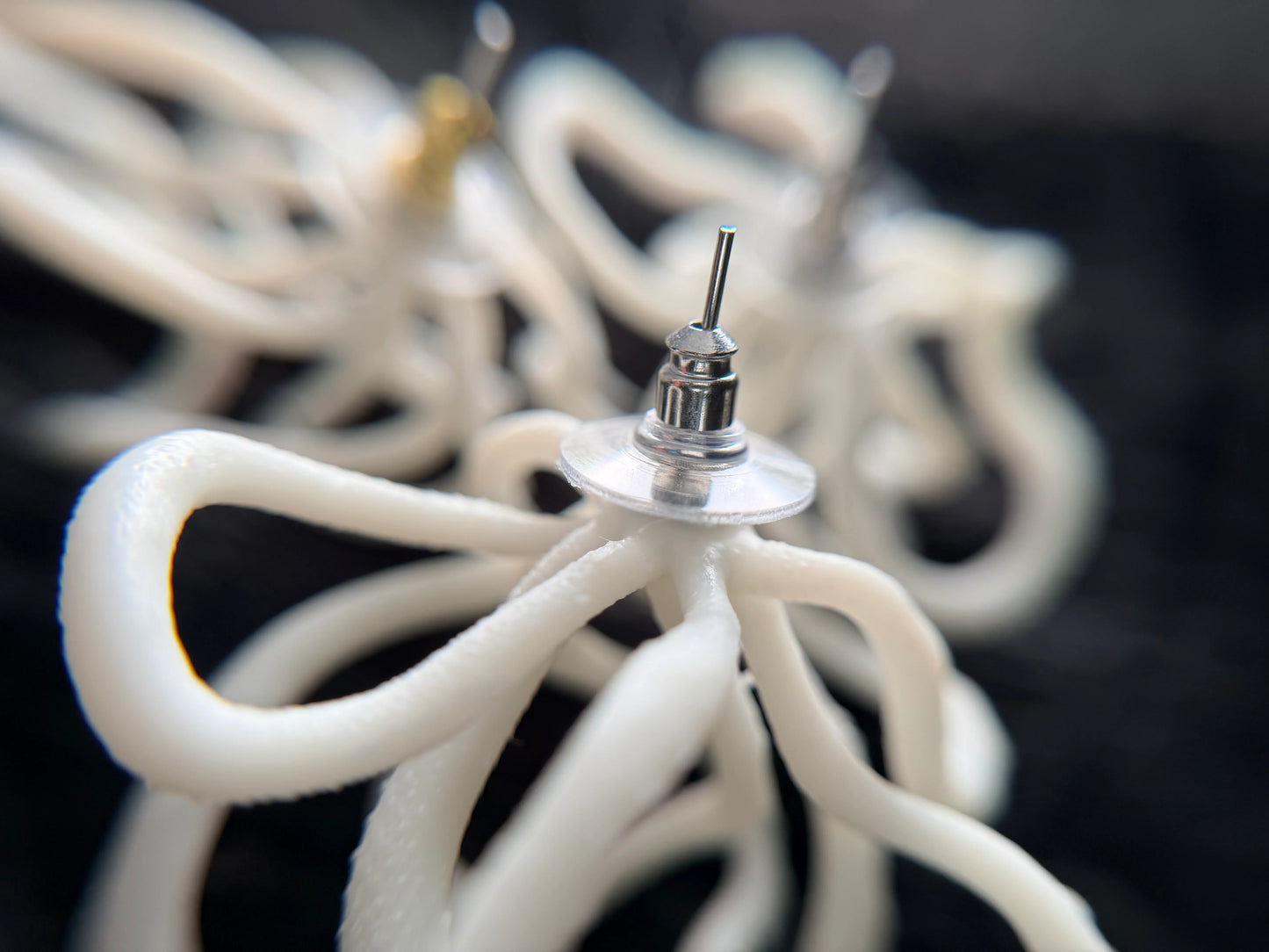 Close-up of sculptural white handcrafted earring by Eclipse Element on dark background