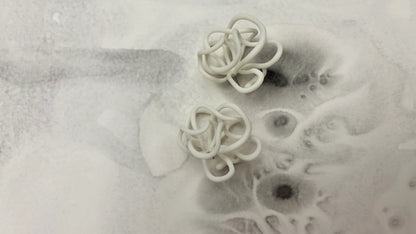 Handcrafted sculptural white earrings by Eclipse Element on abstract grey background