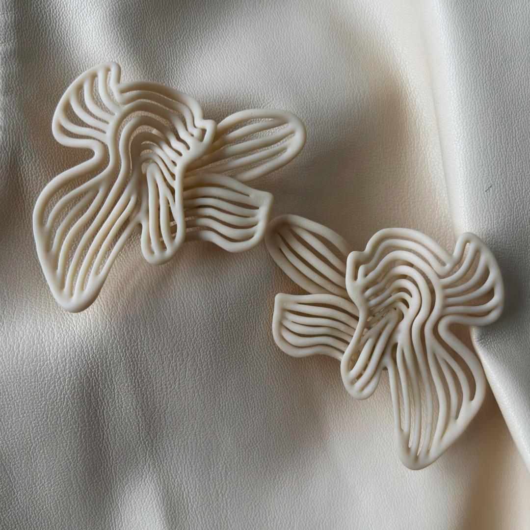 Rhythm Beige sculptural earrings displayed as a pair on a neutral textile background