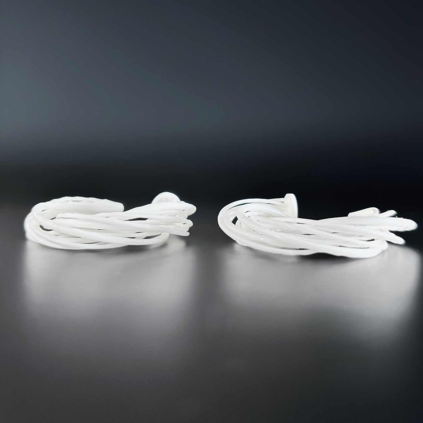 Two large white 3D printed Swirl Hoop Earrings, resting side-by-side on a dark, reflective surface.