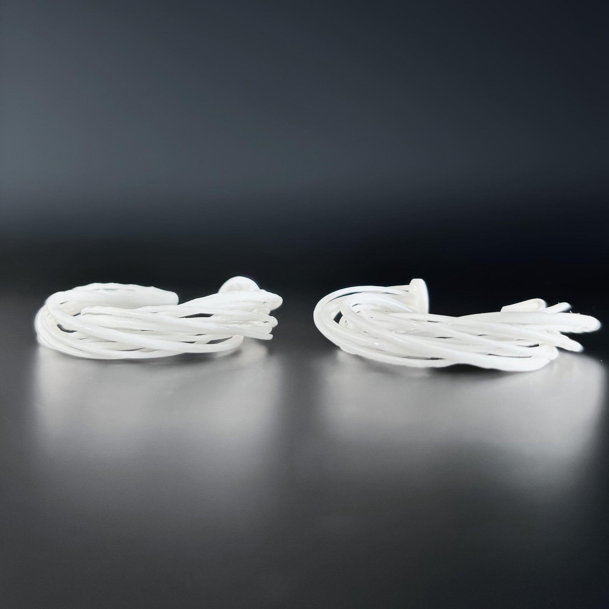 Two large white 3D printed Swirl Hoop Earrings, resting side-by-side on a dark, reflective surface.