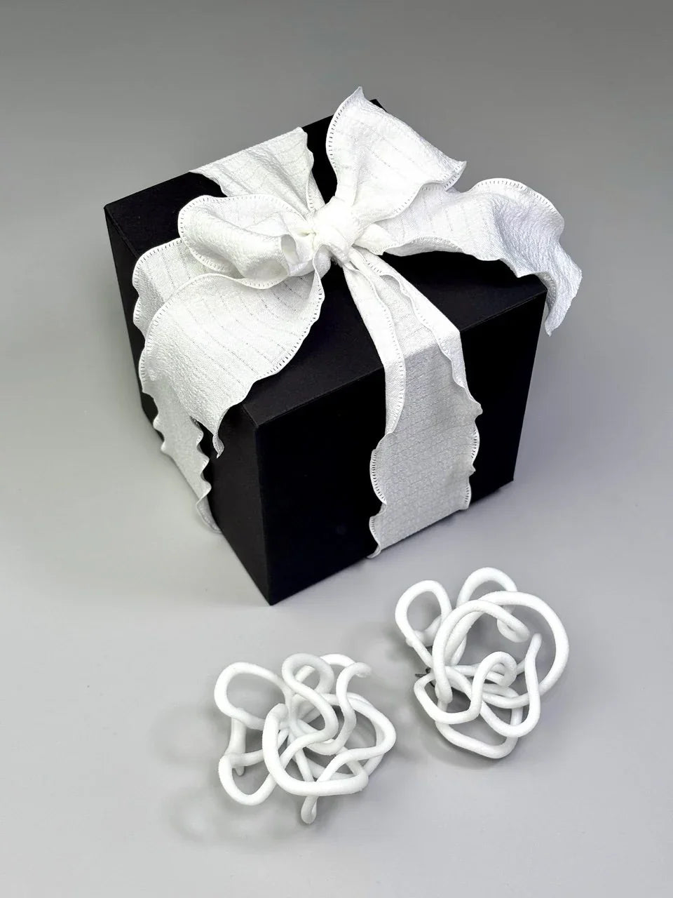 Sculptural white jewelry knots beside a black gift box with a white ribbon, Eclipse Element