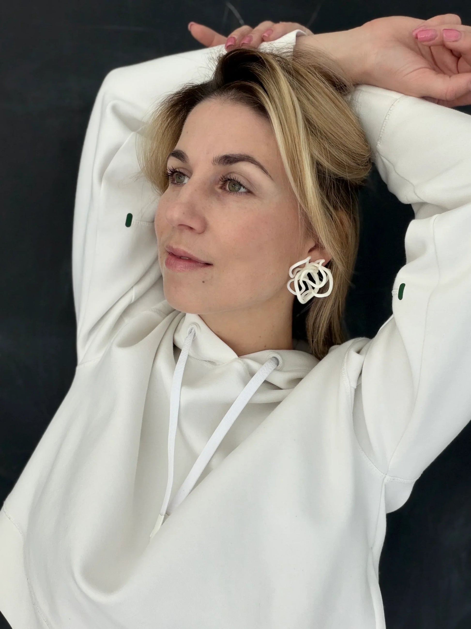 Woman wearing sculptural white earrings and a white hoodie, Eclipse Element jewelry