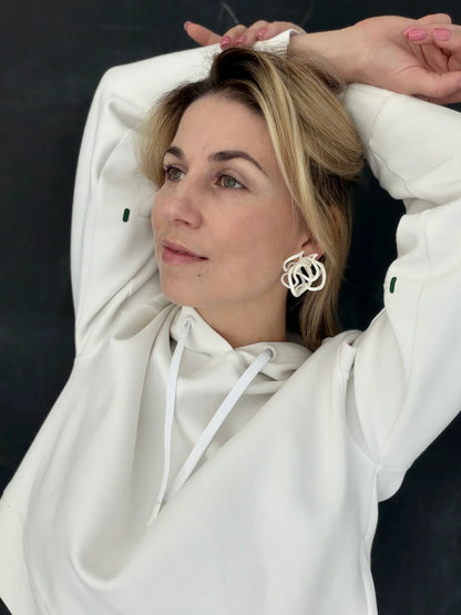 Woman wearing sculptural white earrings and a white hoodie, Eclipse Element jewelry