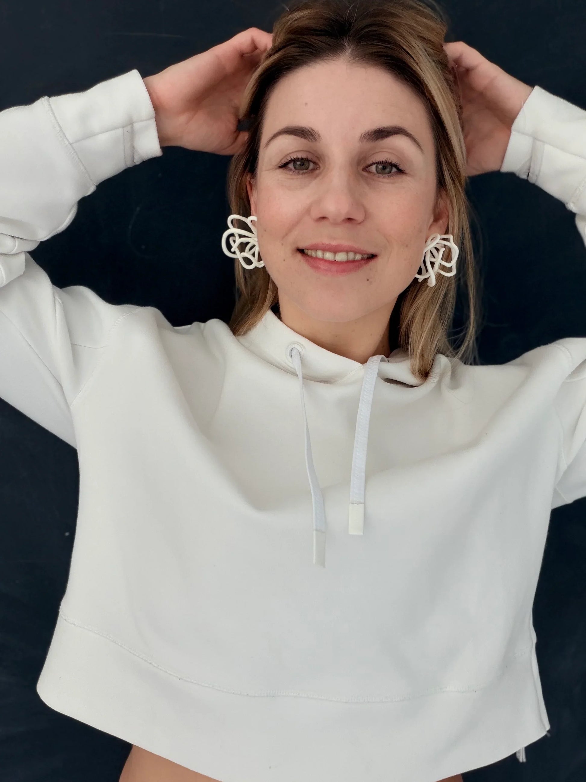 Woman wearing sculptural white earrings and white hoodie, Eclipse Element jewelry style
