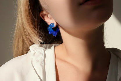 Close-up of a person wearing blue earrings with a blurred background