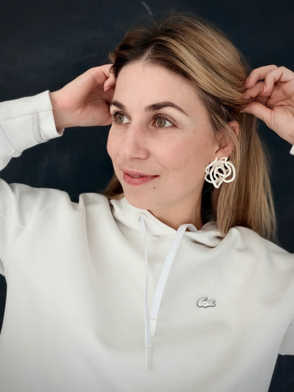 Woman wearing sculptural statement earrings from Eclipse Element, white hoodie, neutral background