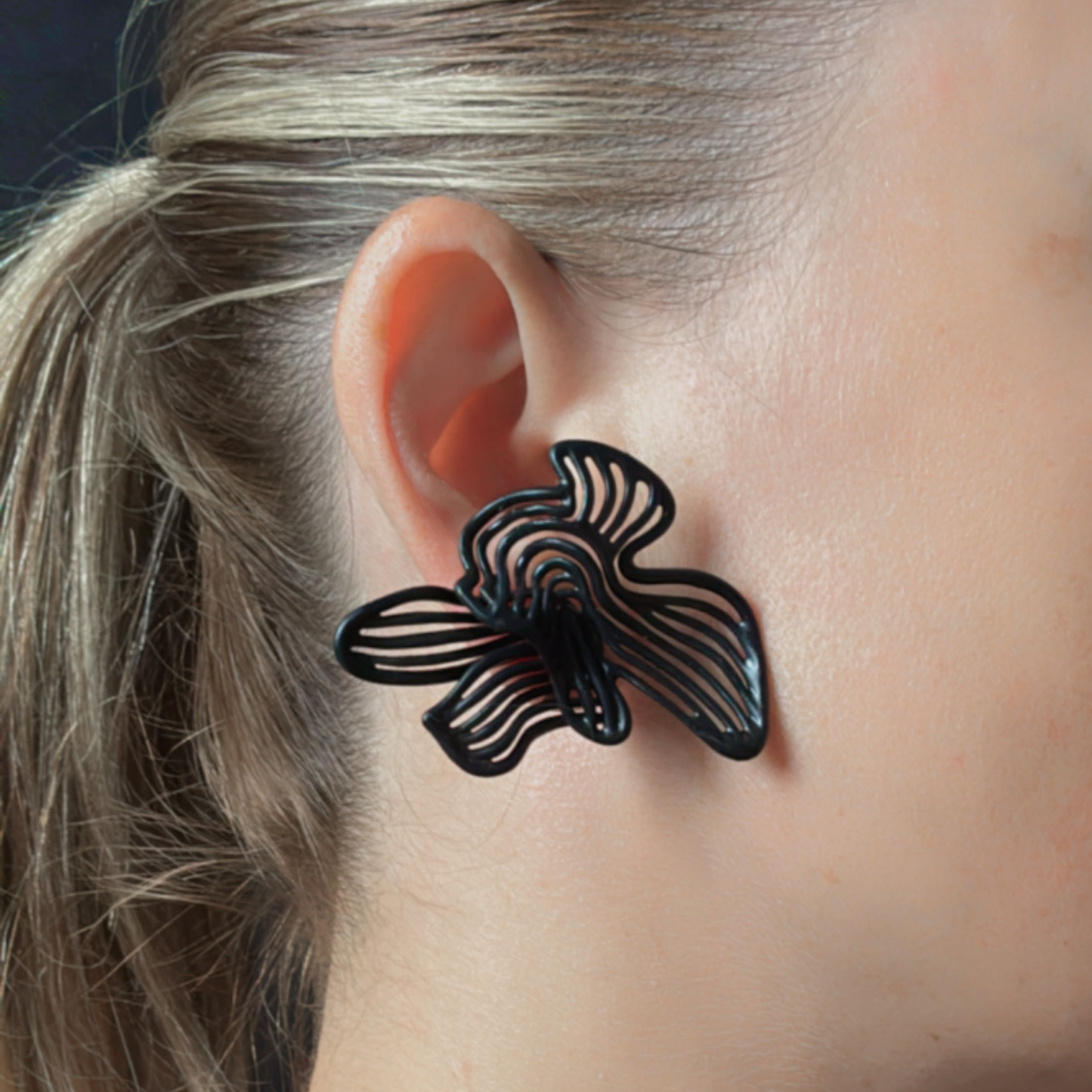 Black floral earring worn by a person with blonde hair.