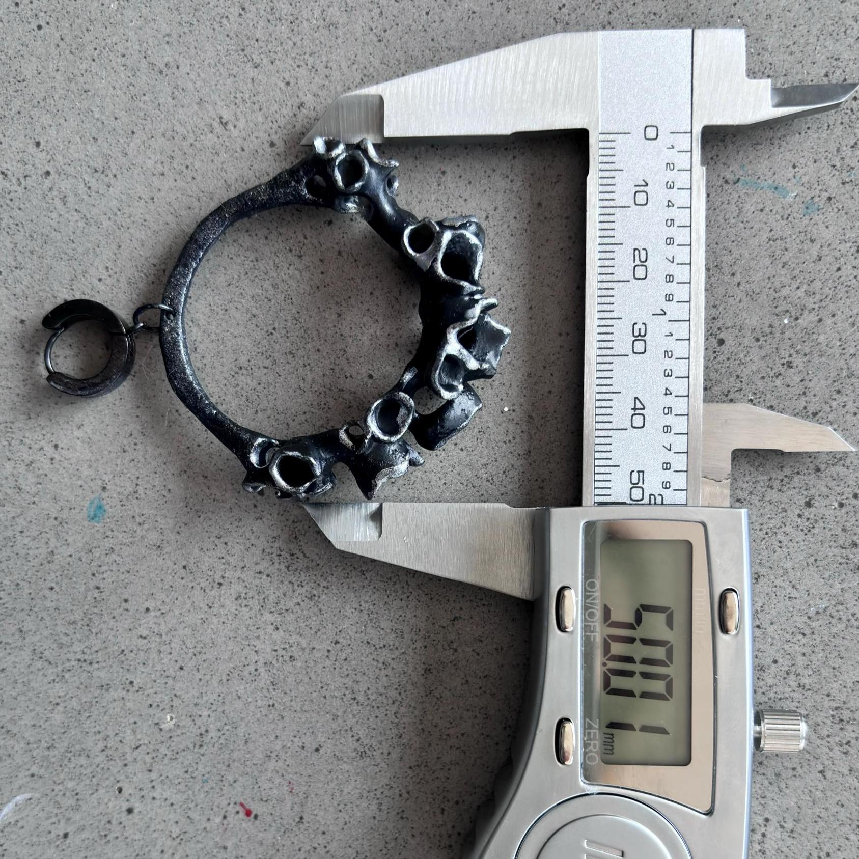 Black  hoop statement earring being measured with a digital caliper on a concrete surface.