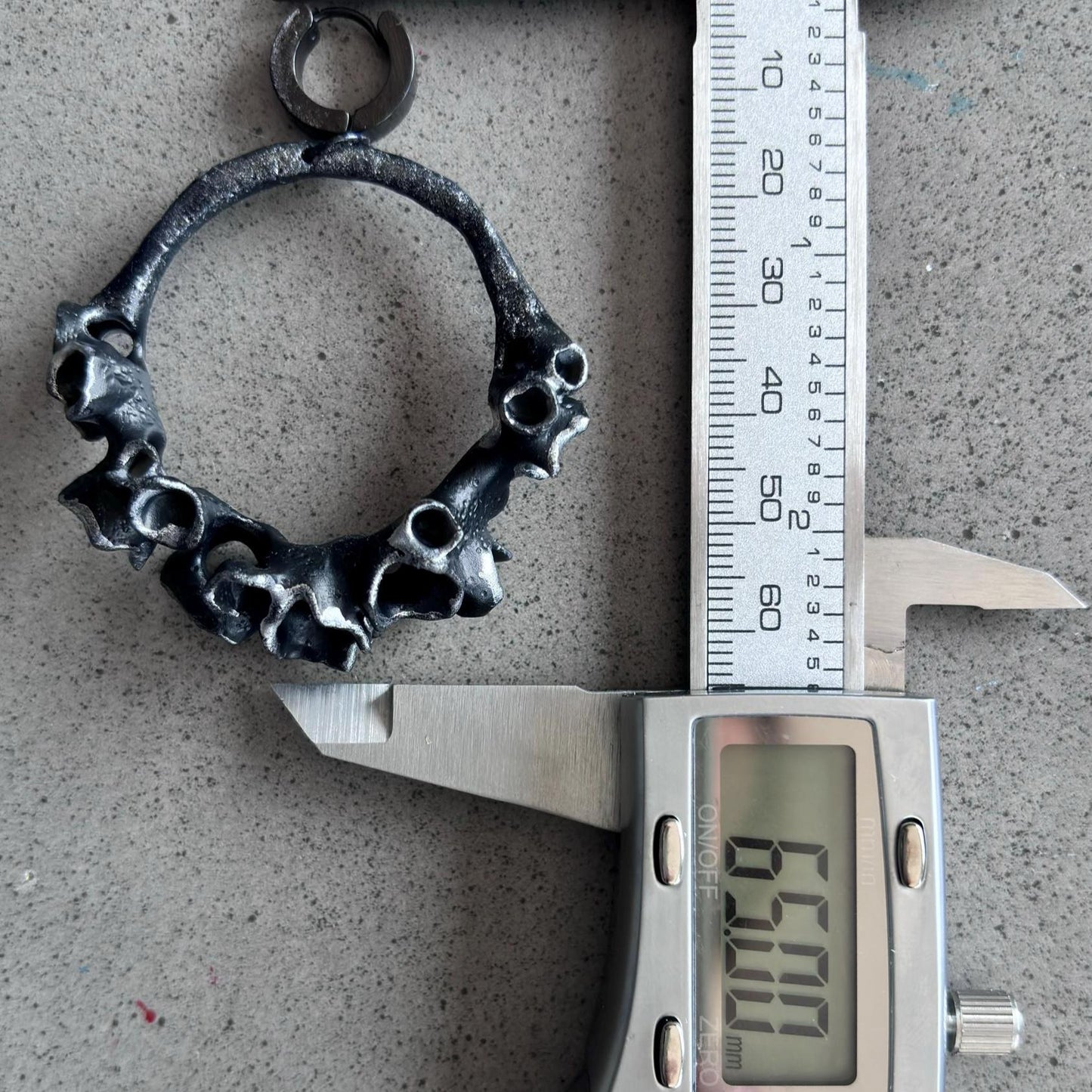 Black  hoop sculptural earring with organic designs being measured by a digital caliper.