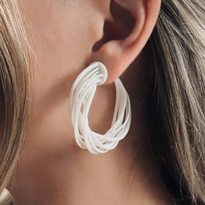 Close-up of a model's ear, showcasing a large white 3D printed Swirl Hoop Earring with a layered, dynamic design.