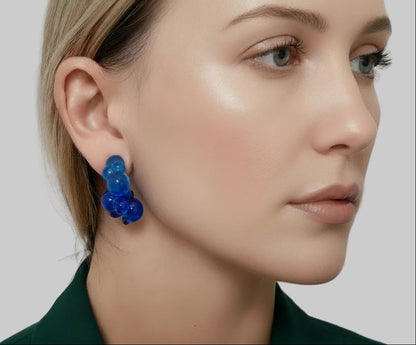 Blue earrings worn by a person with a neutral background