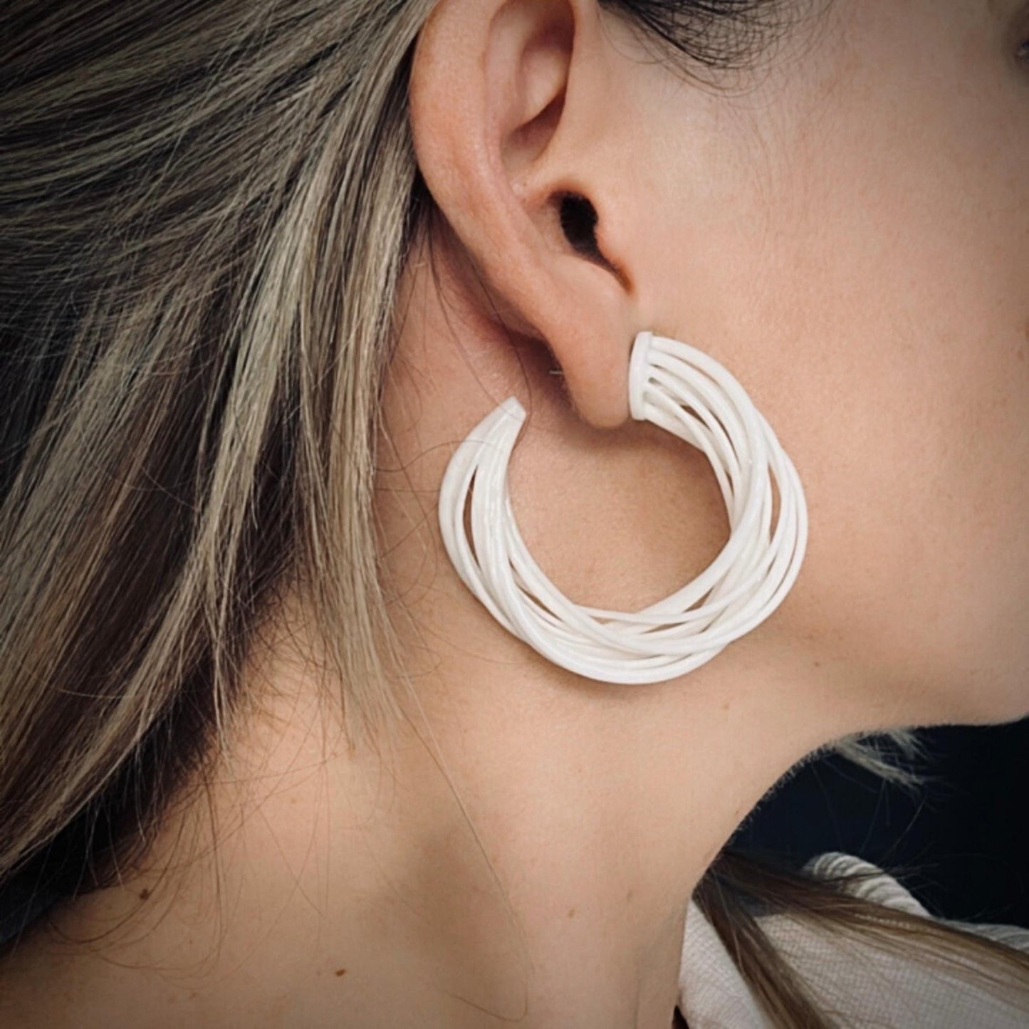 A model wearing a white top, viewed in profile, demonstrating a large white 3D printed Swirl Hoop Earring with focus on the ear.