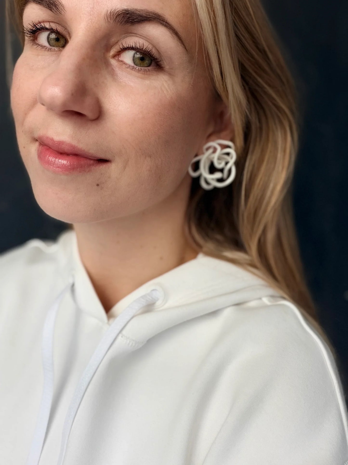 Woman wearing sculptural handcrafted white earrings by Eclipse Element, white hoodie, close up
