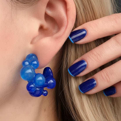 Blue earrings worn by a person with matching nail polish.