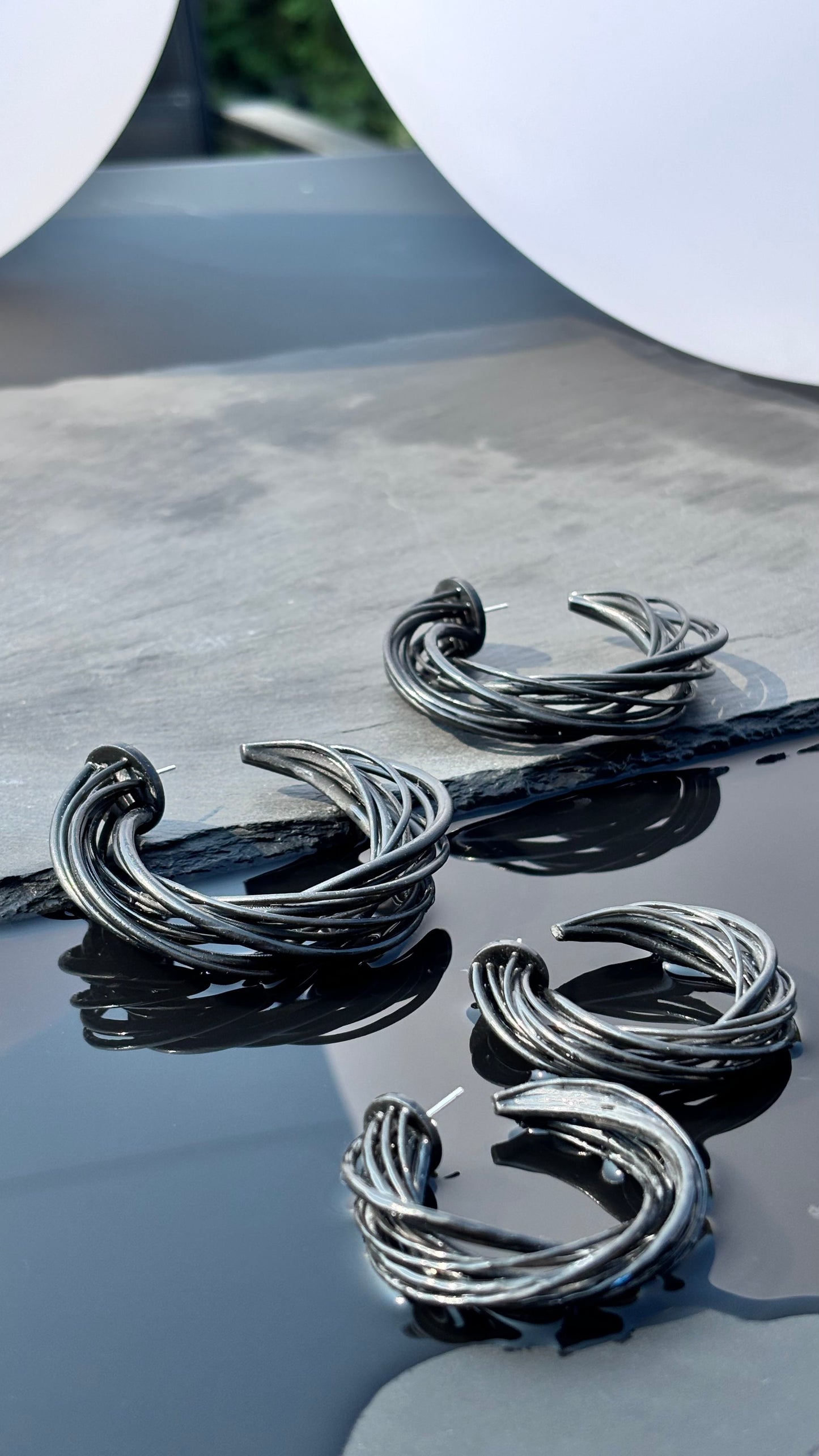 black hoop earrings on a reflective surface with a blurred background