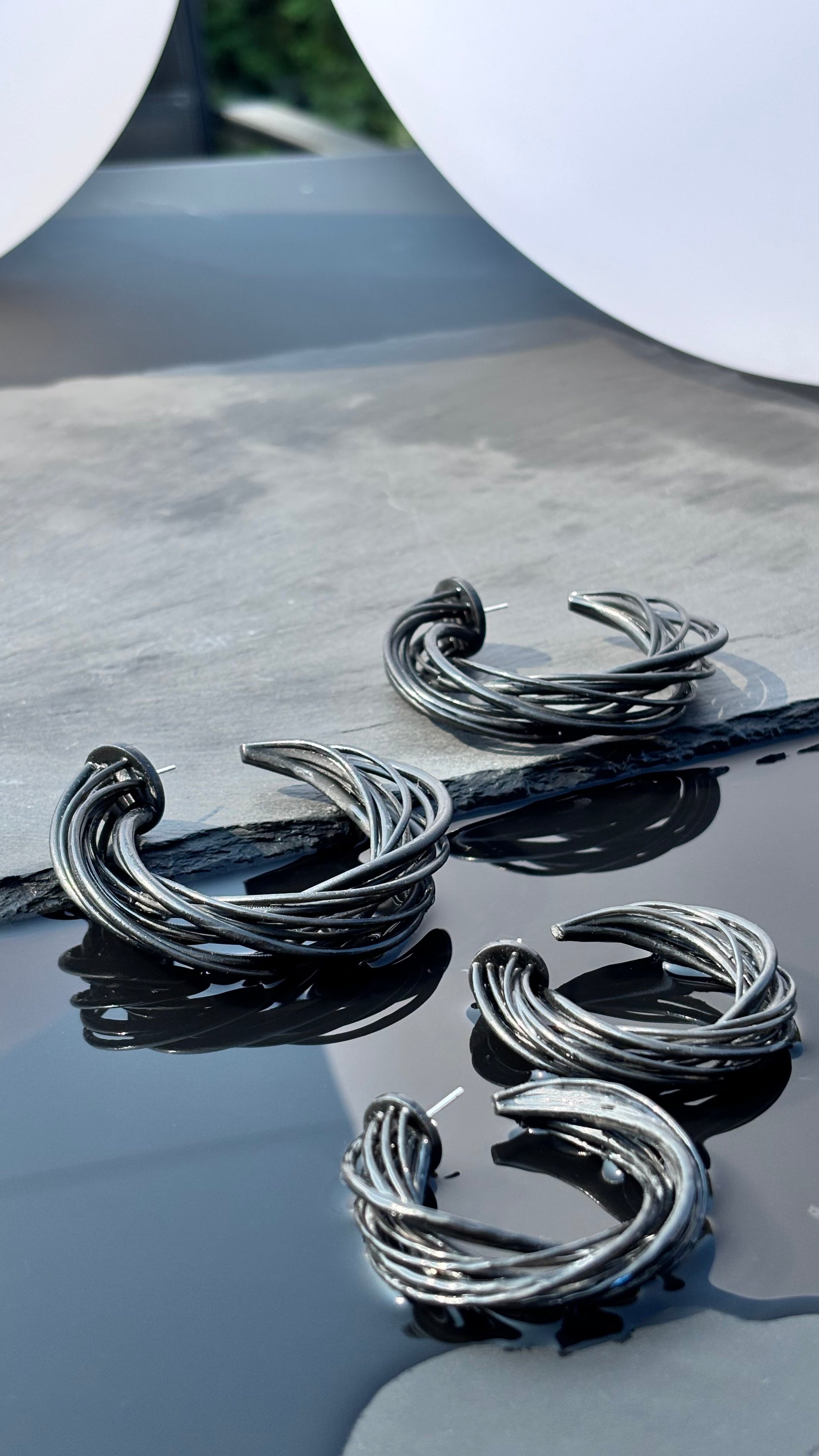 black hoop earrings on a reflective surface with a blurred background