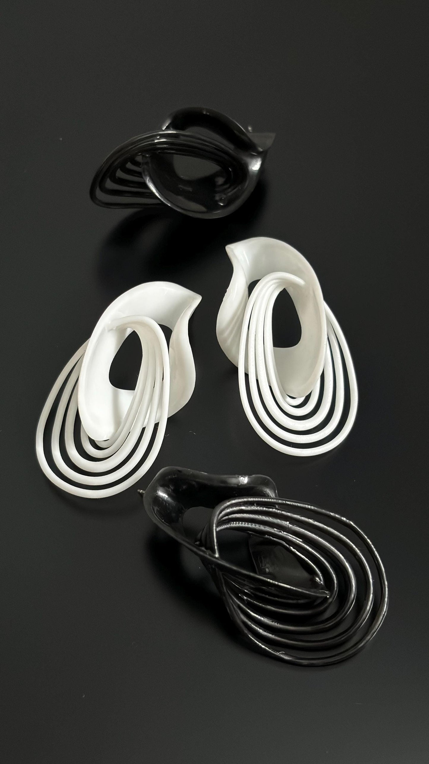 A pair of sculptural drop earrings in white and black, with a fluid, architectural design, displayed against a dark background.