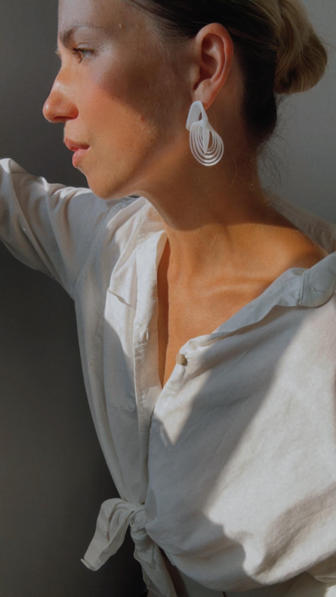Woman wearing white Infinity Loops Statement Earrings and a white shirt, side profile.