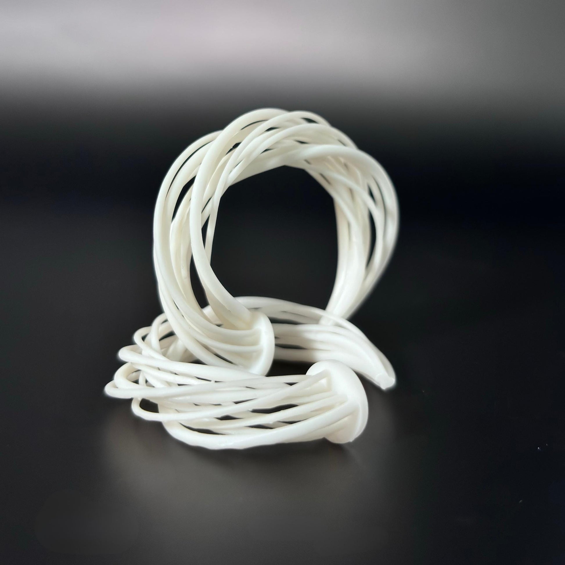 A white 3D printed Swirl Hoop Earring, shown resting on its side, highlighting its curved and layered form against a dark background.