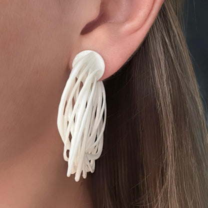 Close-up of a model's face, showcasing a large white 3D printed Swirl Hoop Earring from the side, highlighting the layered texture.