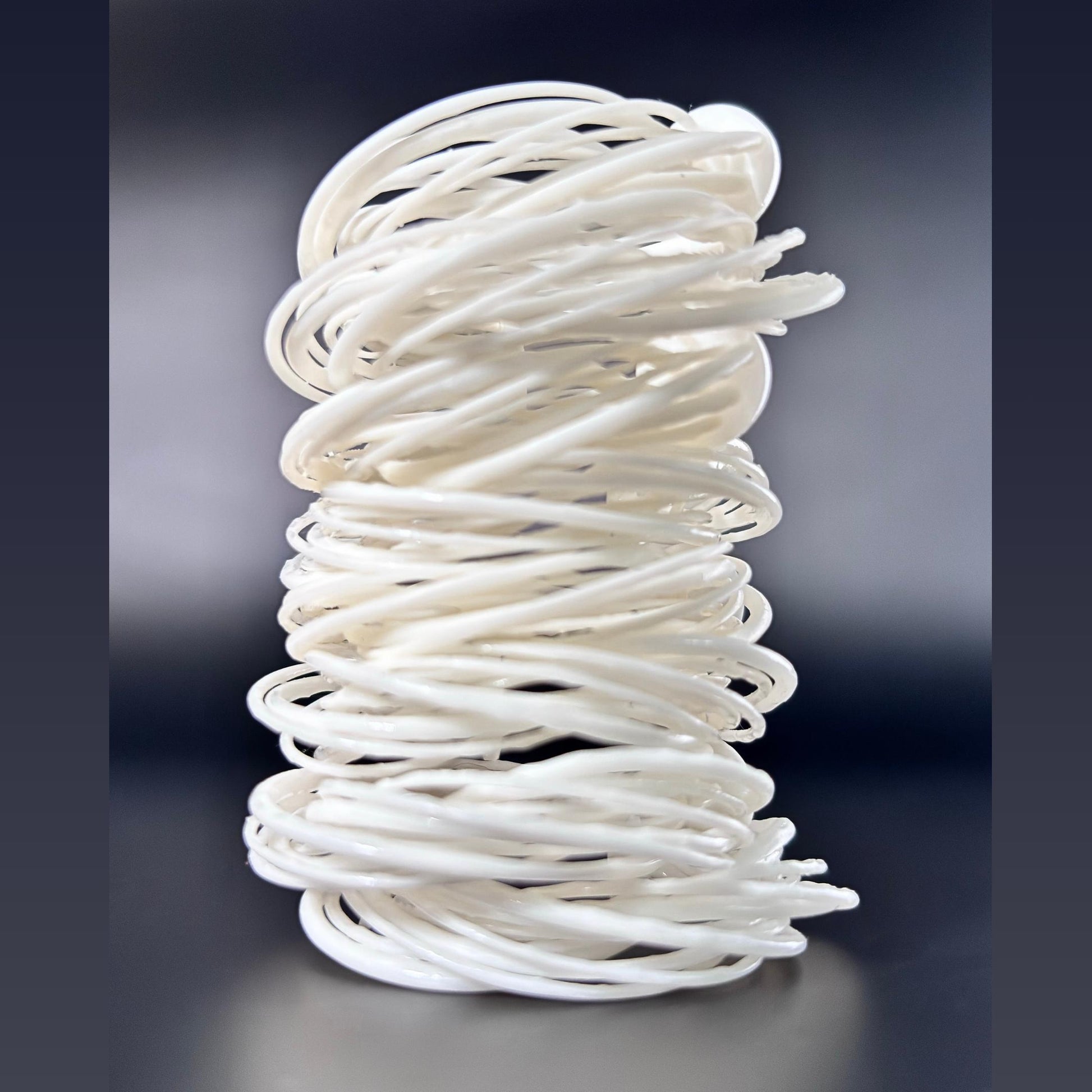 A white 3D printed Swirl Hoop Earring displayed standing upright, showing its layered, cylindrical form, against a dark background.