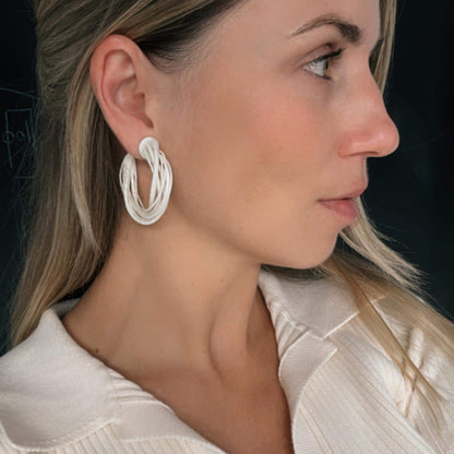 A model wearing a white satin top, viewed in profile, demonstrating a large white 3D printed Swirl Hoop Earring on her ear.
