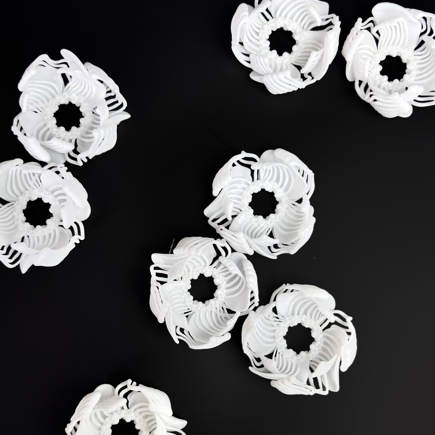 A composition of several black and white 3D printed stud earrings with a layered, geometric pattern, arranged on a black background.