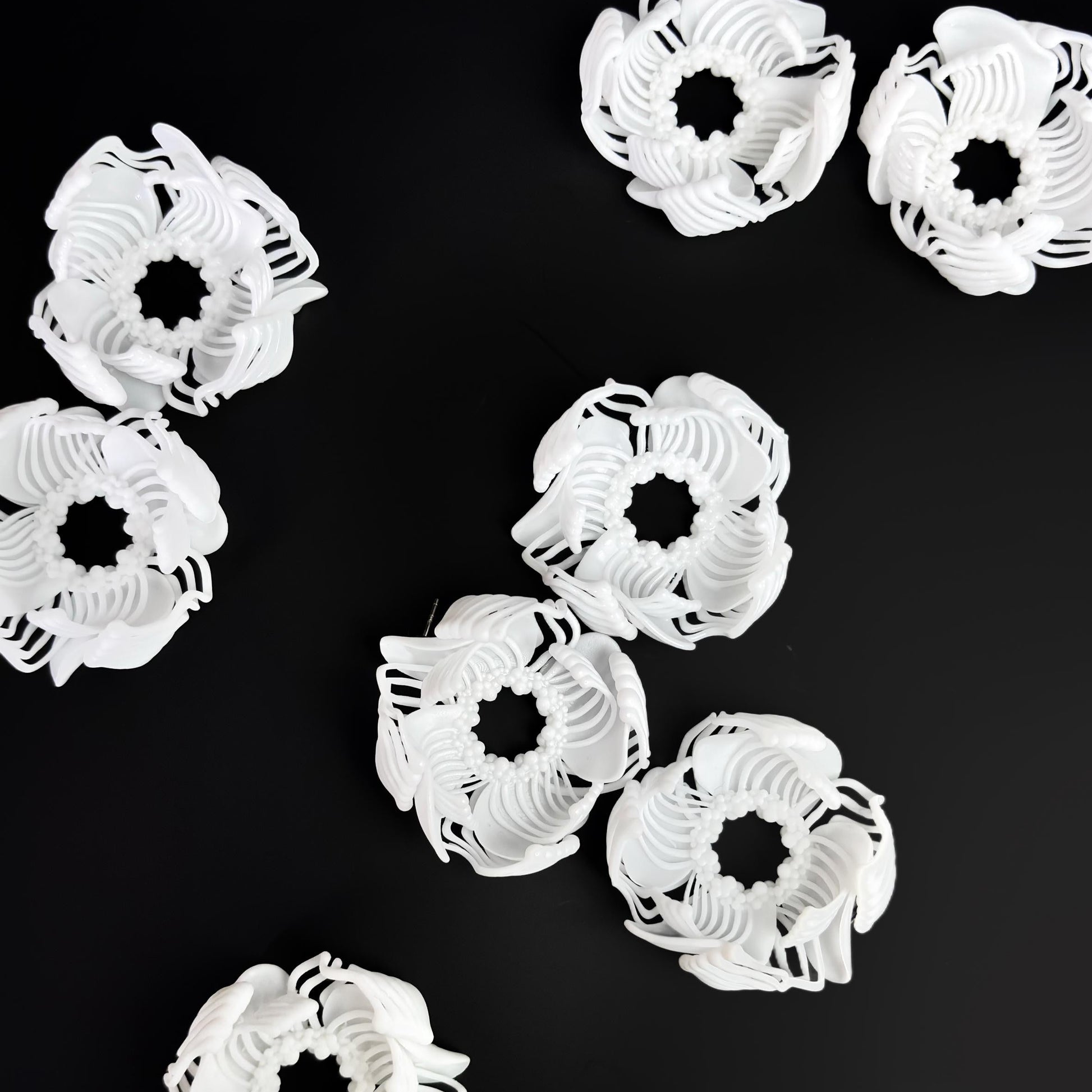 A composition of several black and white 3D printed stud earrings with a layered, geometric pattern, arranged on a black background.