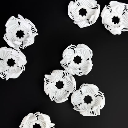 A composition of several black and white 3D printed stud earrings with a layered, geometric pattern, arranged on a black background.