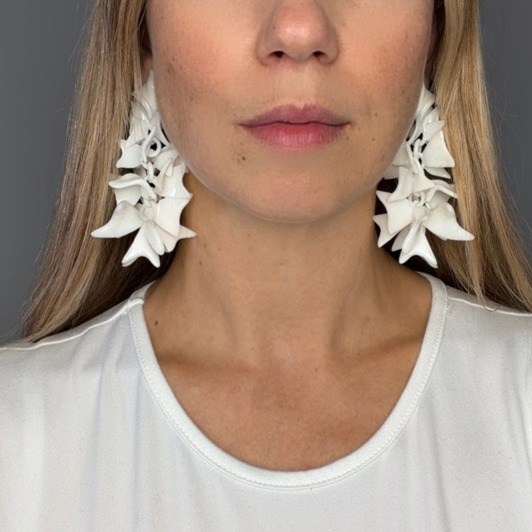 Close-up of a person wearing large white floral earrings with a neutral background