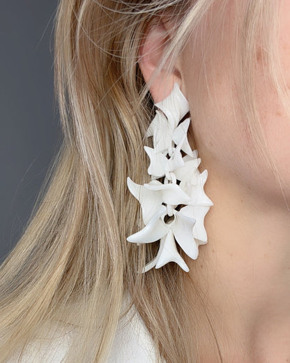 White large petal cascade earrings worn by a person with blonde hair against a neutral background