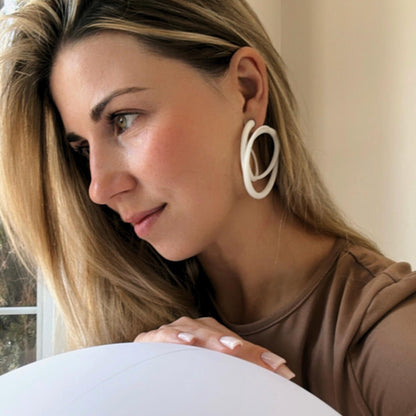 Model with thoughtful expression wearing minimalist white swirl sculptural hoops