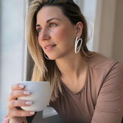 Model in natural light wearing white swirl hoops with light brown top