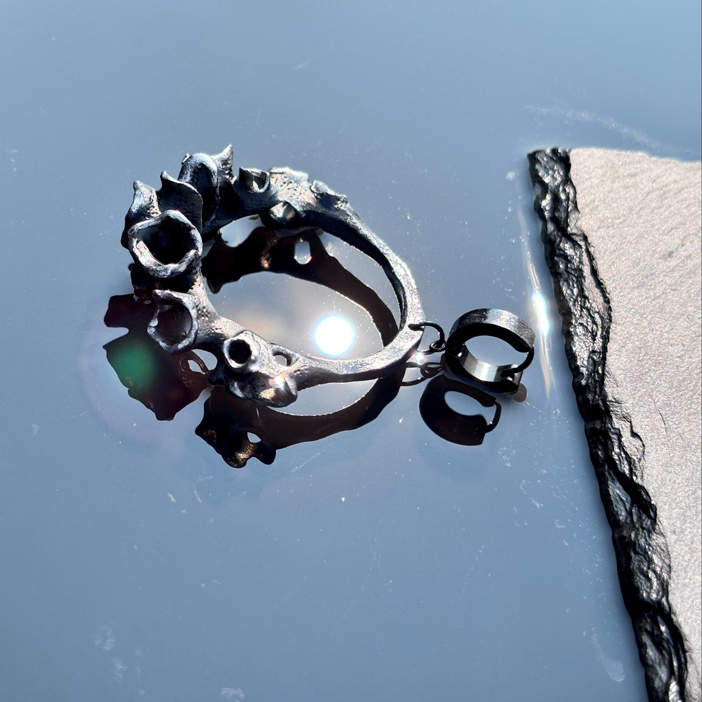 black hoop statement earring with floral and animal designs on a blue background.