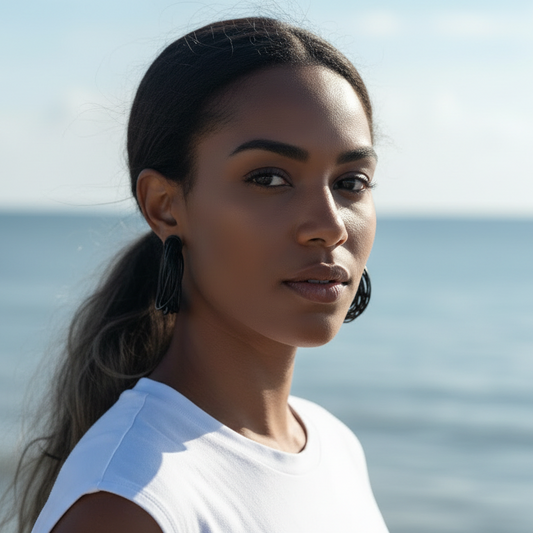 Woman wearing sunglasses and a white top with a blurred ocean background