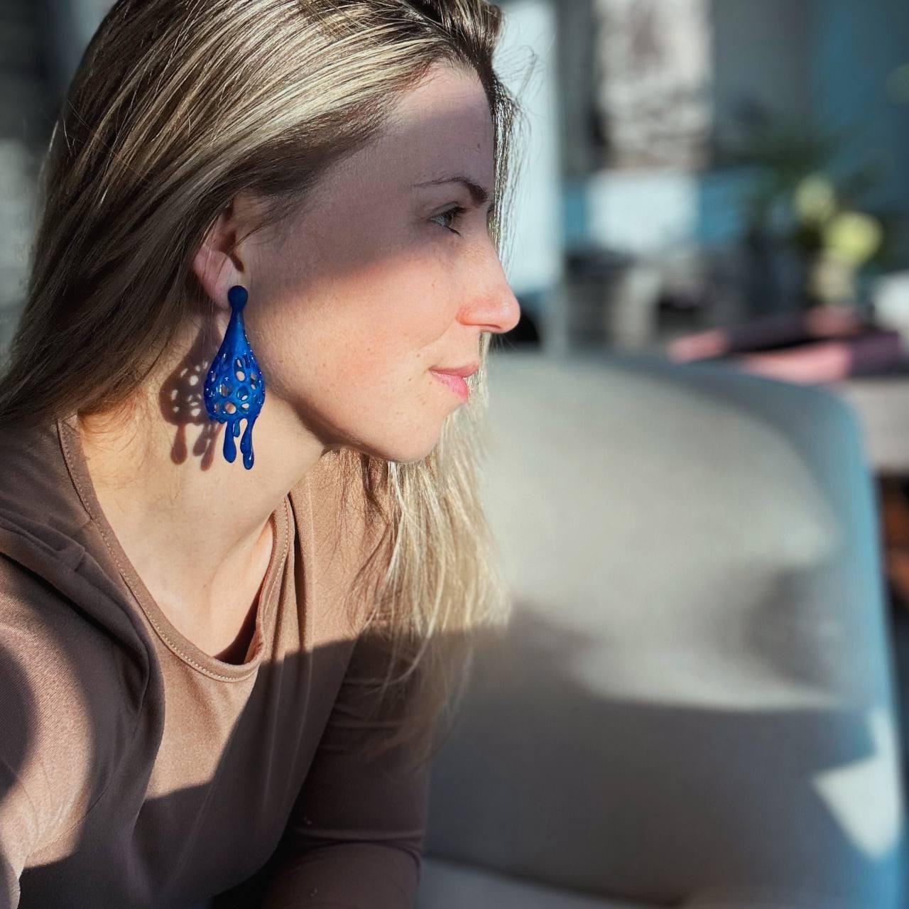 Woman wearing blue earrings looking out a window.