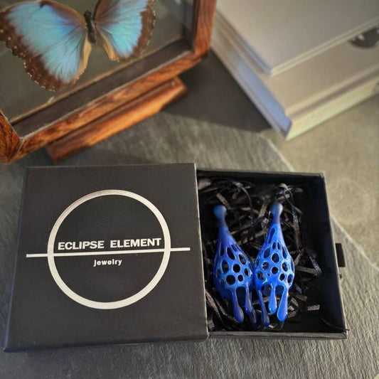 A pair of blue sculptural drop earrings made of 3D printed blue resin, displayed in an open black box with 'ECLIPSE ELEMENT jewelry' printed on the lid.