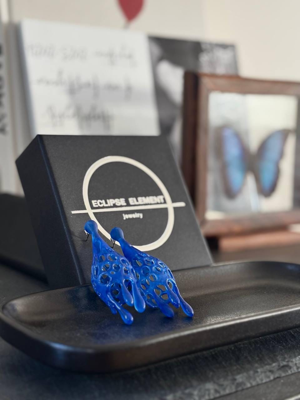 Blue jewelry piece on a black stand with a blurred background.