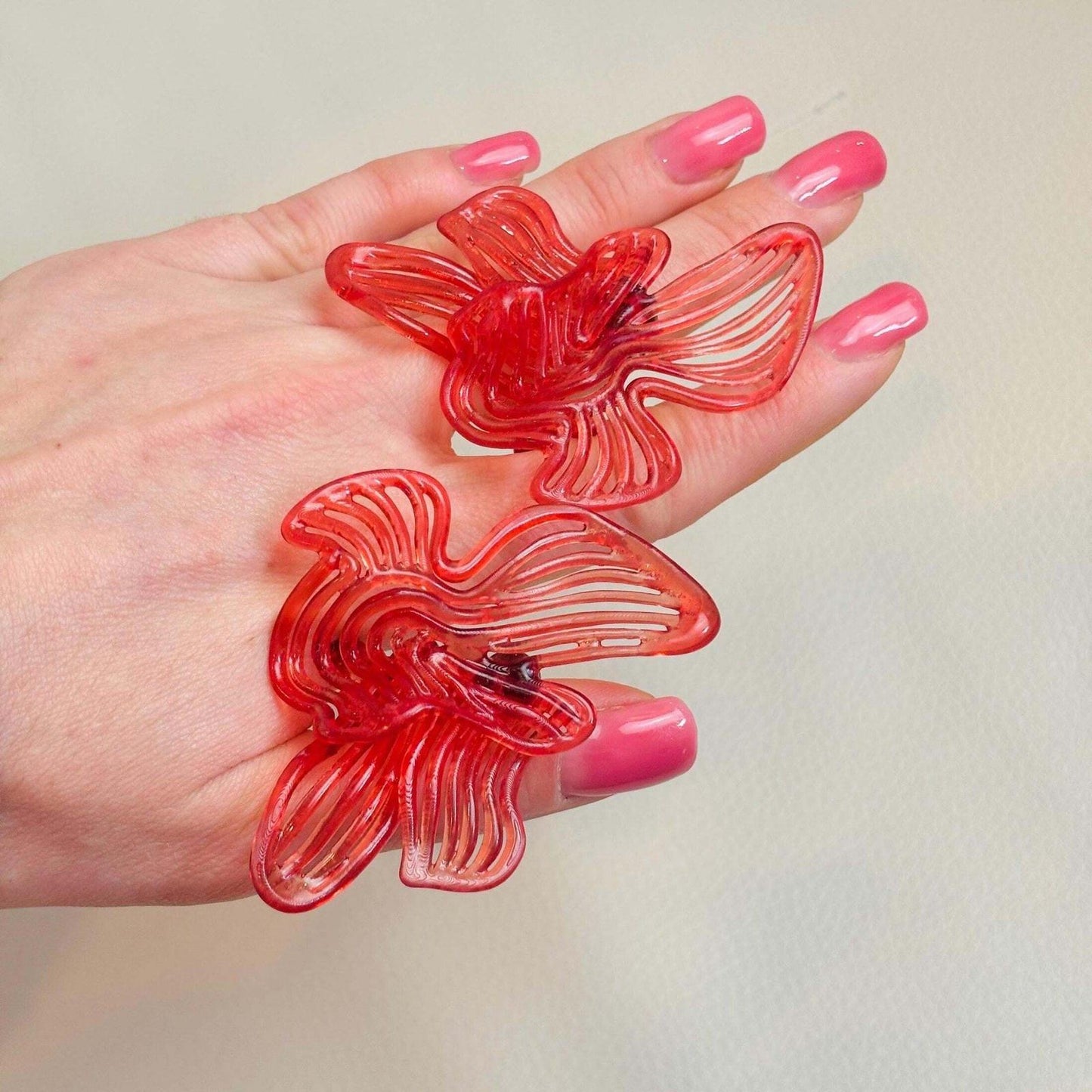 Two earrings held on hand, demonstrating the lightweight feel and size of the red designer jewelry.