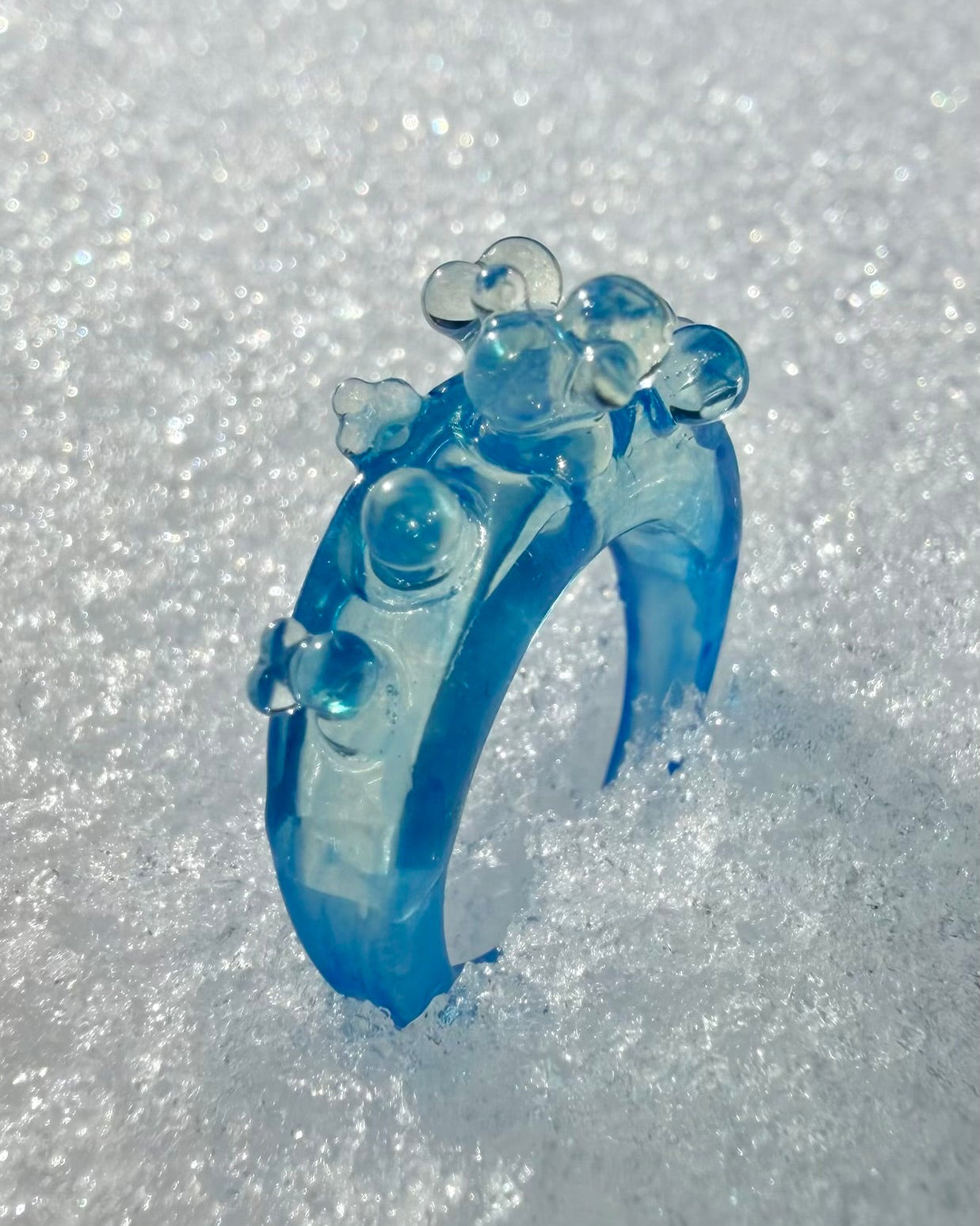 A chunky ice blue sculptural ring worn on a finger, demonstrating its bold architectural size and modern style.