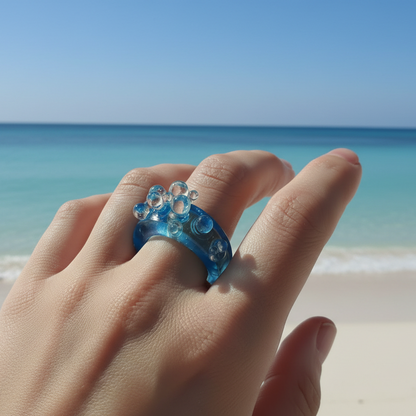 Hand wearing a blue ring with bubble design on a white background