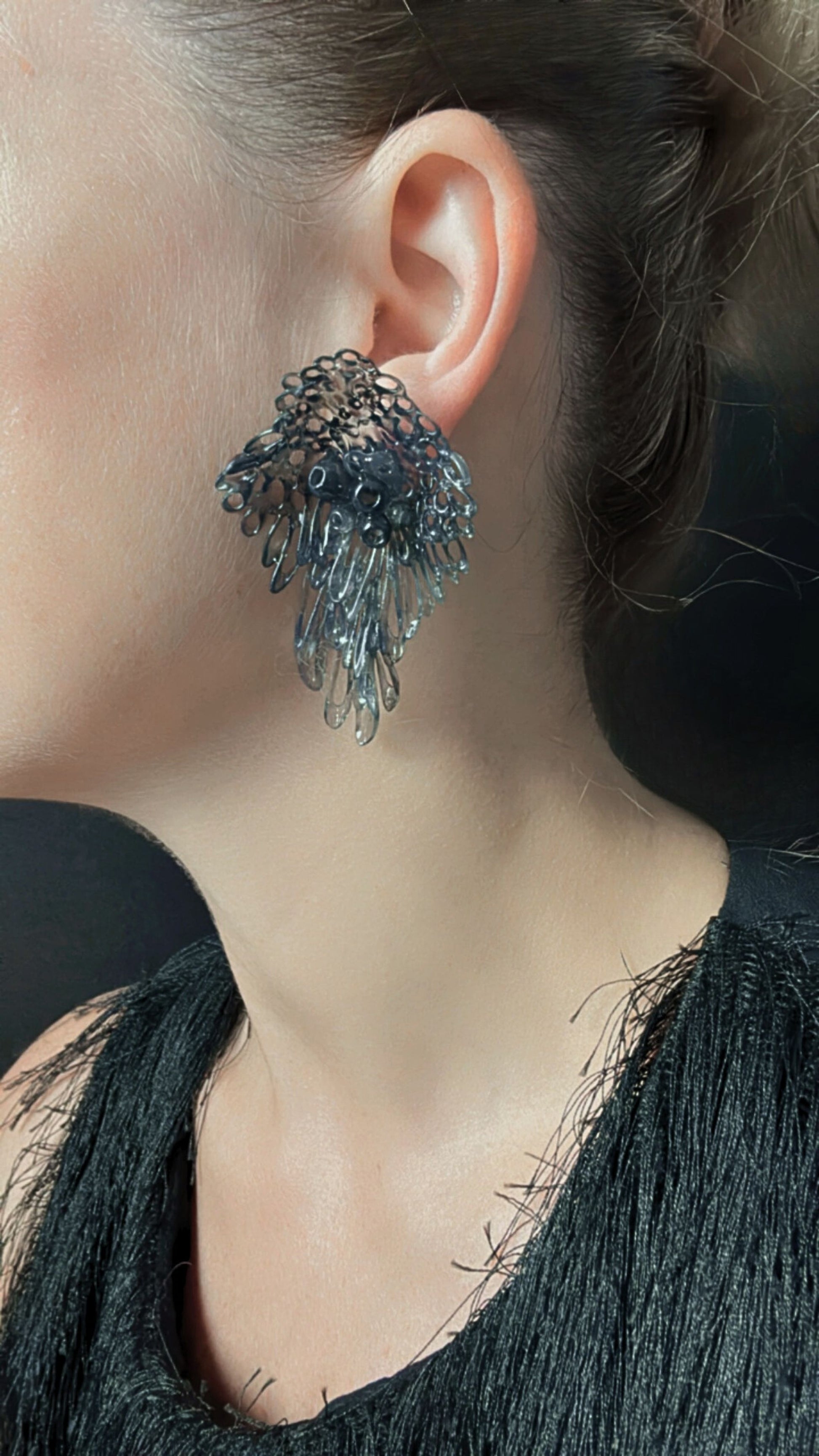 Model wearing black sculptural earrings, clean side view against dark clothing