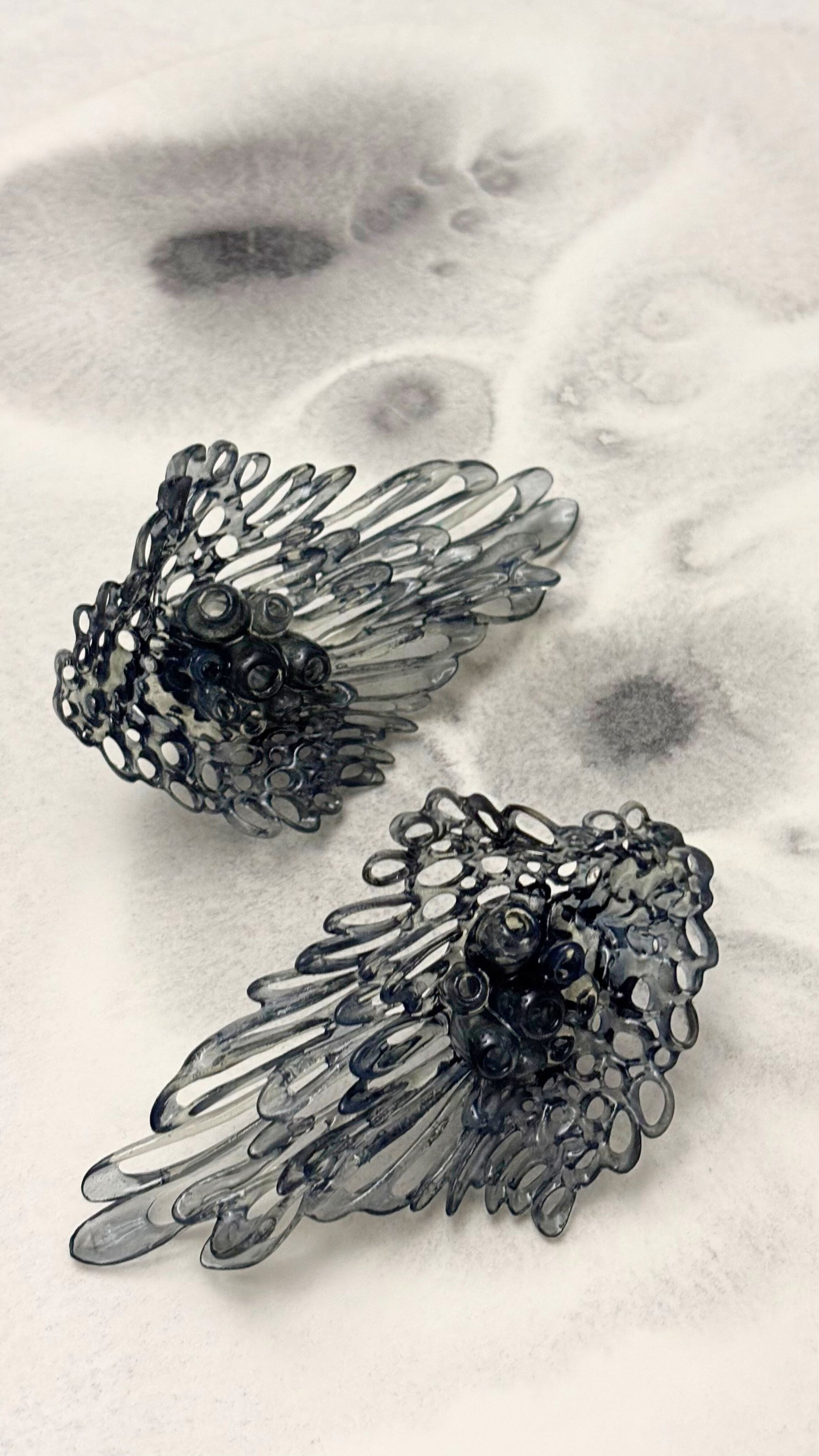 Pair of black sculptural earrings laid flat, emphasizing their intricate lace-like texture